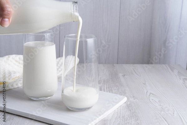 Obraz Pouring homemade kefir, buttermilk or yogurt with probiotics. Yogurt flowing from glass bottle on light background. Probiotic cold fermented dairy drink. Trendy food and drink. Copy space