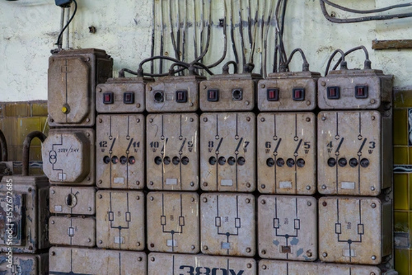 Fototapeta Old industrial electrical switchboard with multiple fuses and switches mounted on a wall. A gritty scene from a factory interior, perfect for illustrating industrial heritage, electrical systems, and 
