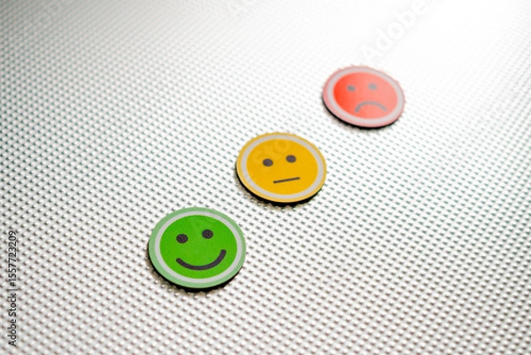 Fototapeta Three round emoji faces in red, yellow, and green representing sad, neutral, and happy emotions on a metallic textured background, symbolizing feedback or mood scale, selective focus in the green one