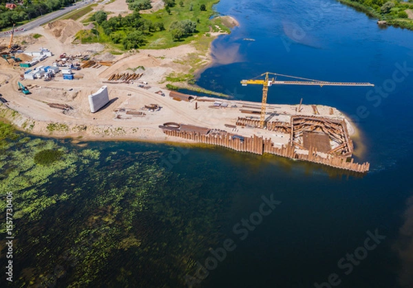 Obraz Construction site of new modern bridge construction in Kaunas, Lithuania. Aerial drone view of bridge connecting two shores of a river. Work progress
