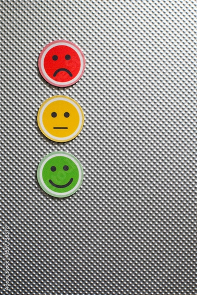 Fototapeta Three round emoji faces in red, yellow, and green representing sad, neutral, and happy emotions on a metallic textured background, symbolizing feedback or mood scale, copy space, vertical