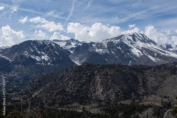 Fototapeta Jagged granite range streaked with late-season snow rises beneath a vivid blue sky criss-crossed by high-altitude jet contrails, illustrating pristine wilderness intersected by modern air routes