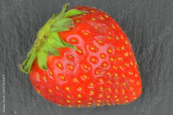 Fototapeta Macro shot of a ripe red strawberry on a black background. Ripe strawberry on a black slate backdrop. Close-up and top view