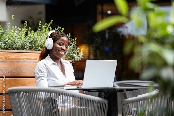 Obraz Happy African black woman in elegant suit sitting in cafe bar and using laptop computer.