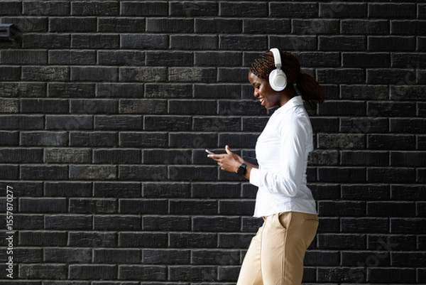 Obraz Beautiful black girl walking by the wall and using smart phone.