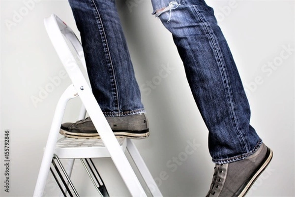 Fototapeta Anonymous man reaching on top of ladder climbing, indoors studio people shot