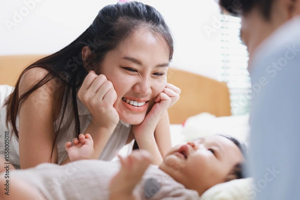 Obraz Happy smiling mother laying down taking care of her little baby son who is sleeping on a white bed. Childcare from birth to 1 year old. Family concept, father, mother, child.