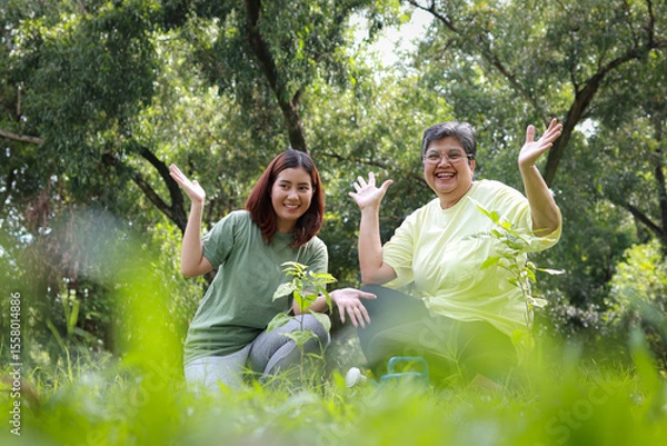 Obraz Volunteer mother and daughter smiling happily are helping to plant seedlings in the forest to help restore the forest. Save the world. Plant trees to reduce global warming. Green ecosystem.