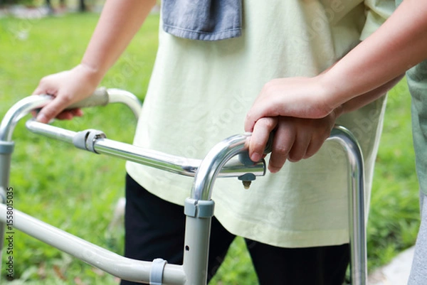 Obraz Close-up view of elderly woman using cane to walk, exercising in outdoor garden with hands of daughter or physical therapist.  Health care center for the elderly.