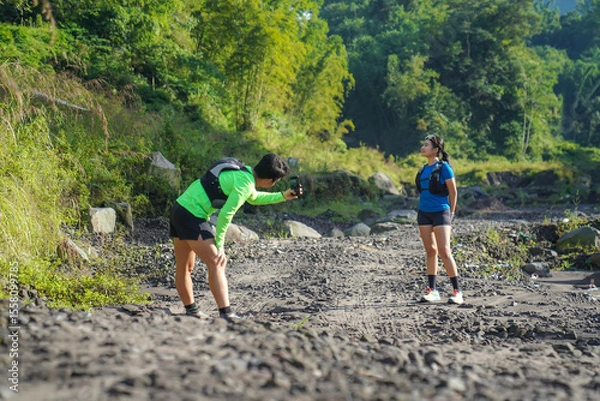 Obraz Asian Couple Trail Running and Taking Photos in Lush Nature Landscape