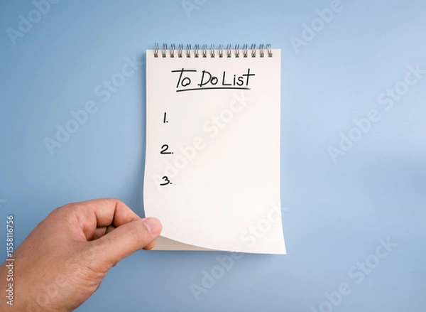 Obraz To do list, planning and checklist concept. "to do list," handwritten text font and list numbers on white page of tear-off memo pad, spiral notepad, opened by person hand, isolated on blue background.