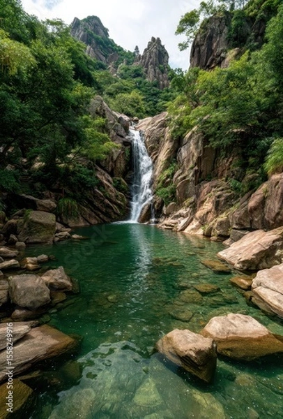 Fototapeta Serene Waterfall Cascading into Crystal Clear Pool Surrounded by Lush Green Trees and Rugged Rock Formations in a Mountainous Landscape