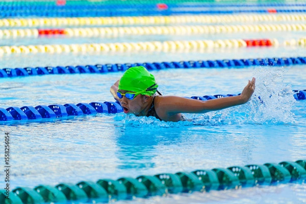 Fototapeta Swimmer child swims butterfly swimming style in a race swimming pool. Water sports and competition, learning to swim classes for children.