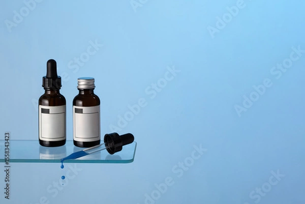 Fototapeta Amber glass serum bottles with dropper and drops on the bath shelf at blue background. Perfect representation of modern skincare, beauty rituals, and cosmetic treatments. Copy space