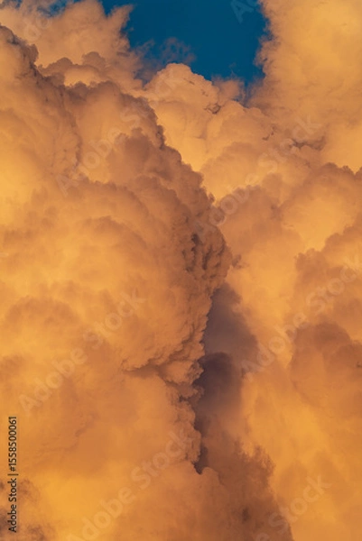 Fototapeta Massive orange thunderclouds illuminated by the evening sun with a deep blue sky peeking through. A dramatic natural scene capturing the power and beauty of the atmosphere.