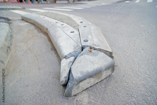 Fototapeta Broken concrete barrier before and after the pedestrian crossing, infrastructure decay, need for road repairs. Damaged concrete block on curved street serves as warning barrier against illegal parking