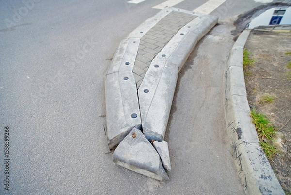 Fototapeta Broken concrete barrier before and after the pedestrian crossing, infrastructure decay, need for road repairs. Damaged concrete block on curved street serves as warning barrier against illegal parking