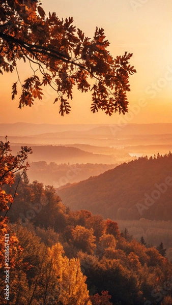 Fototapeta Warm sunlight illuminates layers of colorful trees and rolling hills covered with a blanket of mist during a serene autumn morning, creating a breathtaking natural panorama