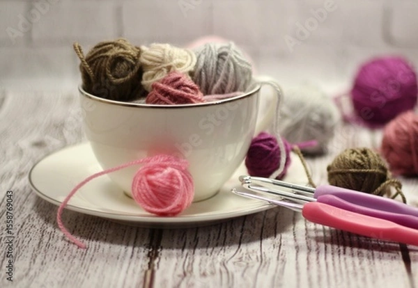 Fototapeta A cup and a saucer with clews balls of yarn wool and crocheted blanket handmade craft bright photo	
