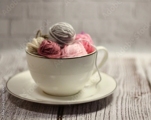 Fototapeta A cup and a saucer with clews balls of yarn wool and crocheted blanket handmade craft bright photo	

