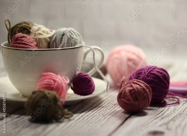 Fototapeta A cup and a saucer with clews balls of yarn wool and crocheted blanket handmade craft bright photo	
