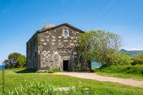 Fototapeta Yason church in Ordu city. Historic stone building set against a backdrop of lush greenery and a serene shoreline. For themes related to history and religion.
