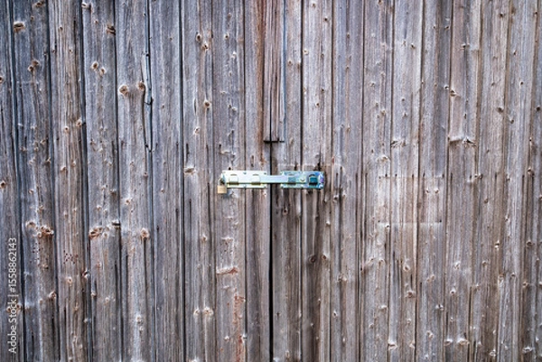 Fototapeta An aged wooden door with rustic metal hinges and deep weathered texture. Old wooden door with lock.