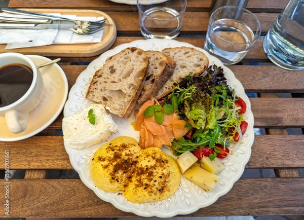 Obraz A savory breakfast served at an outdoor cafe, featuring a generous platter with benedict eggs, salmon, fresh salad, and bread.Close-up of a balanced breakfast meal on a decorative plate