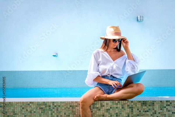 Obraz A woman sitting on the edge of the pool using a laptop