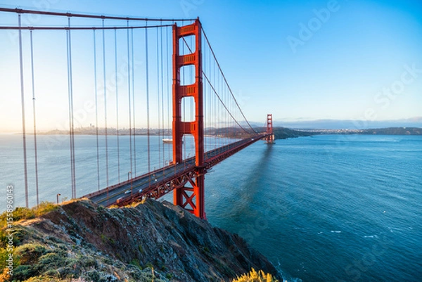 Fototapeta Golden Gate Bridge at sunrise in San Francisco, California. Scenic view from Battery Spencer with soft pastel sky, calm bay waters, and iconic red architecture. Tranquil travel landscape.