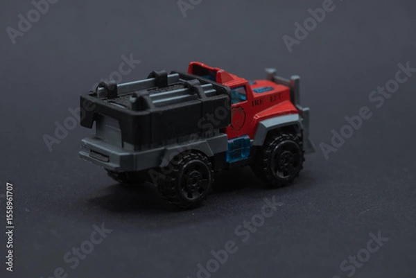 Obraz Toy fire truck on black surface suitable for childrens book illustrations, website graphics, firefighterthemed designs, educational materials. Playful and colorful.