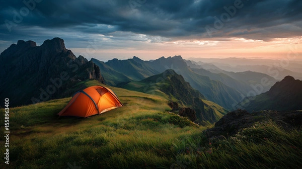 Fototapeta An orange tent stands solitary in a golden meadow at sunrise, with majestic, snow-capped mountains towering in the dramatic alpine background, perfect for adventurous travel and wilderness exploration
