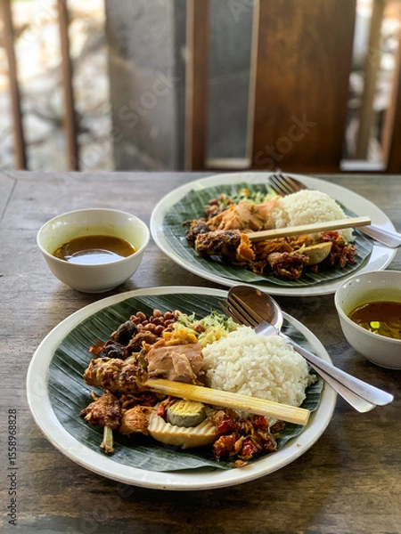 Fototapeta Nasi Campur is a Traditional Balinese rice dish served on a banana leaf with various side dishes, showcasing authentic Indonesian cuisine.