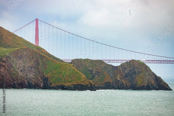 Fototapeta Close-up view of the Golden Gate Bridge rising behind rugged coastal cliffs of Marin Headlands, captured on a moody overcast day in San Francisco Bay, California