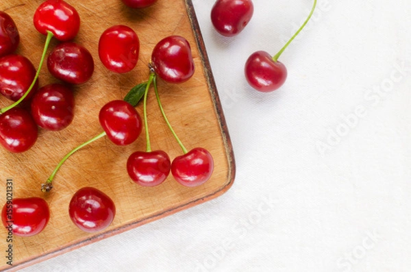 Fototapeta Ripe red cherries on a wooden cutting board on a white background. Concept of summer berry harvest. Horizontal orientation. Selective focus. Top view. Copy space.