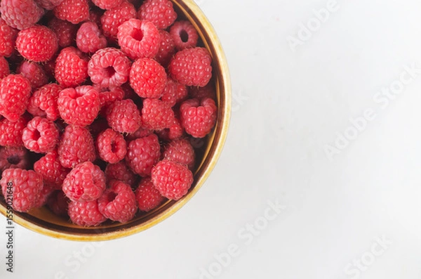 Fototapeta Ripe pink raspberries in a ceramic bowl on a white background. Summer berry harvest concept. Horizontal orientation. Selective focus. Top view. Copy space