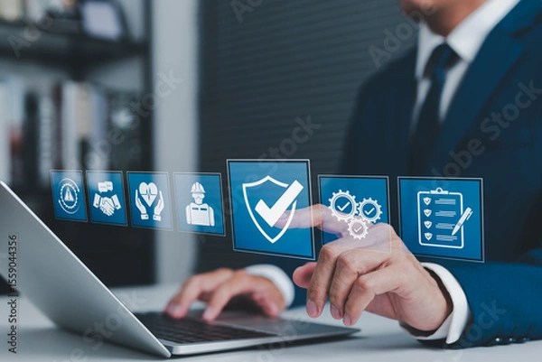 Obraz Work Safety and Compliance Concept. Businessman using laptop with icons safety, compliance, quality control, and risk management, representing workplace safety, regulations, and operational standards.
