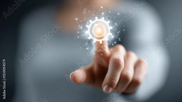 Obraz A person is reaching out to touch a glowing gear icon that represents technology and innovation. The background is blurred, focusing on the digital interaction.