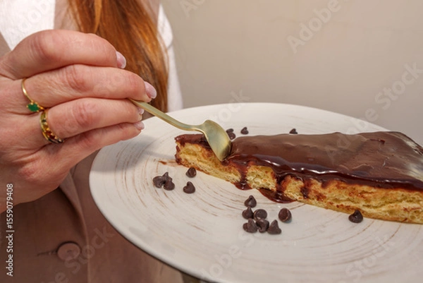 Fototapeta Pastry professional savoring chocolate cake garnished with cocoa chips, golden utensil in hand