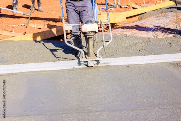 Fototapeta Workers are using concrete leveling tool to smooth out freshly poured cement at construction site.