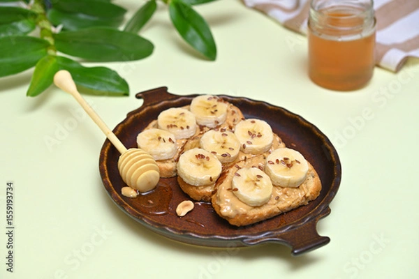Fototapeta vegan toasts with peanut butter, banana and honey on a plate close-up