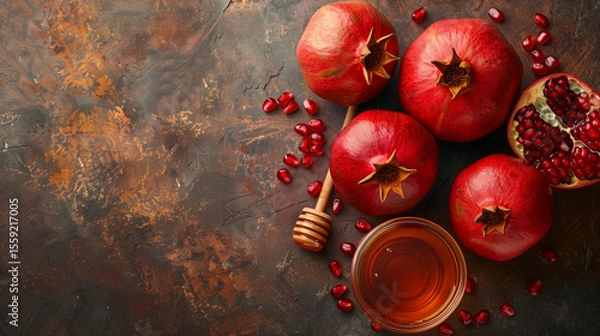 Fototapeta Whole and cut pomegranates with honey dipper on rustic background