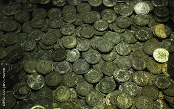 Fototapeta A pile of Polish 1 grosz coins, mostly dark and aged, with one shiny coin standing out, illuminated under moody lighting.