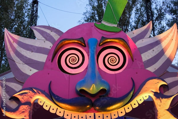 Fototapeta Surreal entrance to a funfair attraction with a colorful, hypnotic face featuring spiral eyes and exaggerated features.