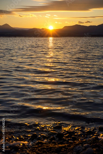 Fototapeta Beautiful sunset over the mountains above the lake. Reflection of sun rays in the water in a sea bay with trees