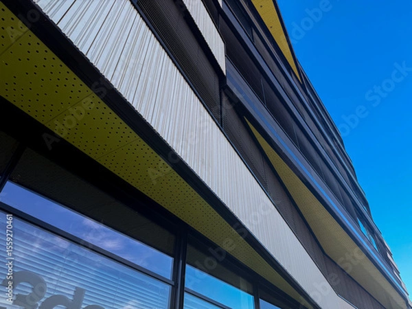 Fototapeta Modern architectural building facade with geometric patterns and vibrant colors against blue sky