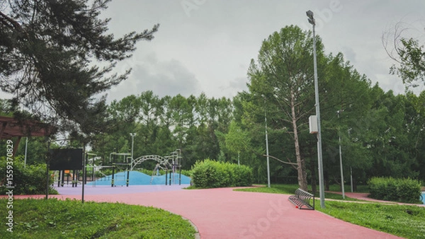 Fototapeta Modern outdoor playground with colorful rubber surface and climbing structures surrounded by trees, concept of childhood, recreation and urban nature