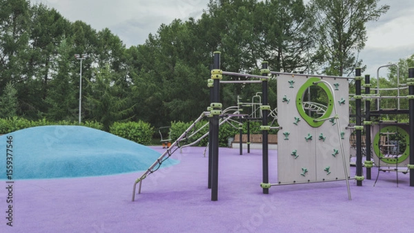 Fototapeta Colorful modern playground with climbing walls, rope structures and a blue hill on a vibrant purple surface, surrounded by greenery, concept of childhood fun and physical development