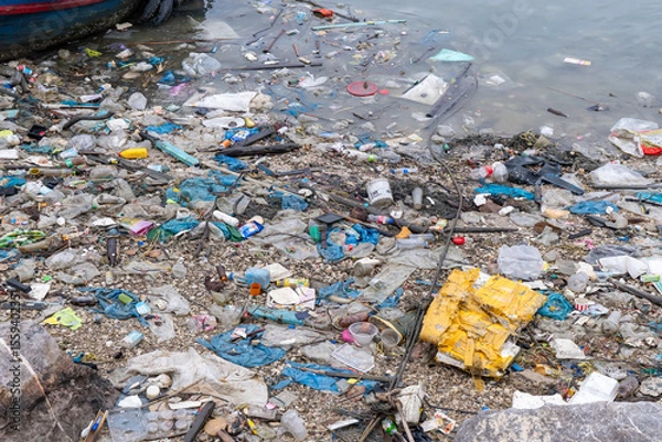 Fototapeta Pollution crisis at riverside exposed as debris accumulates along the shoreline during a cloudy afternoon