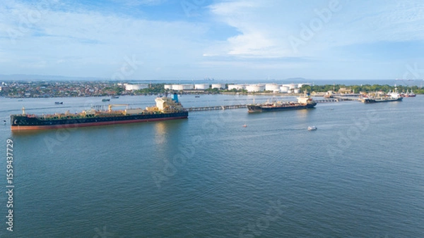 Obraz Oil tanker docked at Cilacap refinery with large storage tanks, suitable for energy industry websites, transportation logistics, and education resources.